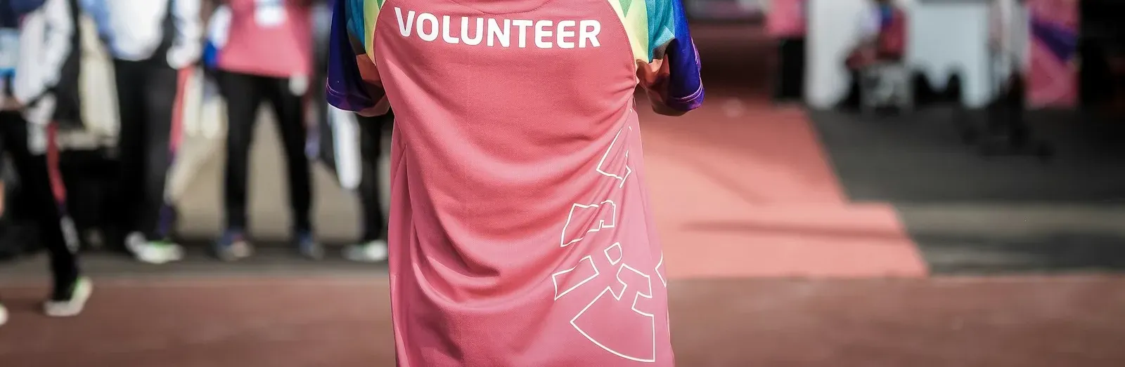 Vrijwilliger in sporttenue met "Volunteer" op de rug, van achteren gezien op een evenement