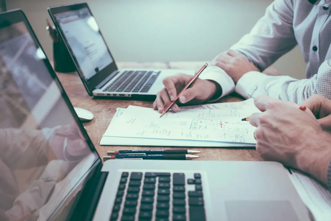 Twee mensen nemen cijfers door op papier, met laptops op tafel